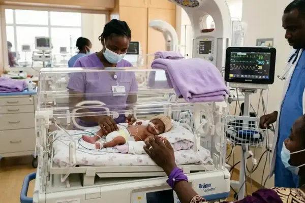 A premature African newborn receives specialized care in a neonatal intensive care unit while healthcare professionals monitor the baby's condition and a parent gently holds the infant's hand through the incubator, highlighting the importance of quality care for premature babies.