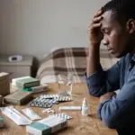 Young man with malaria medicines and multiple antimalarial packages representing uncertainty about treatment and fake malaria medicines.