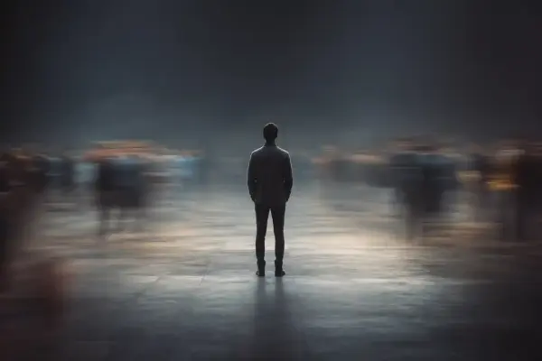 A sharply focused person stands alone with their back to the viewer as blurred crowds move around them, symbolizing the isolation associated with stigma.