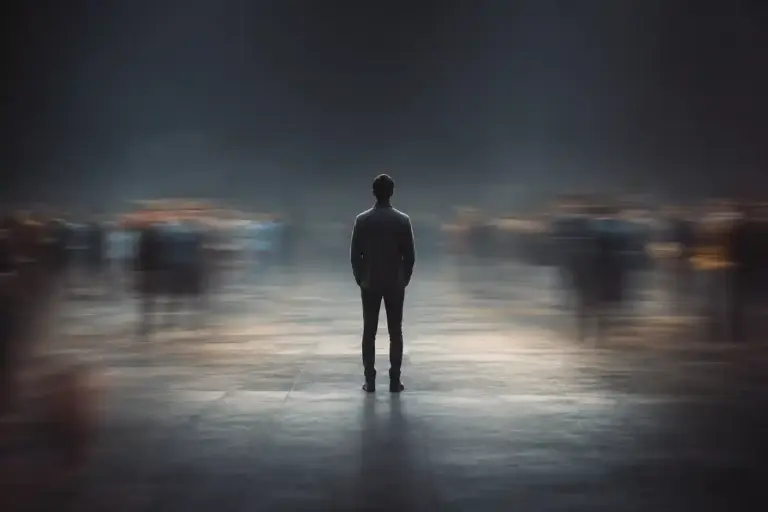 A sharply focused person stands alone with their back to the viewer as blurred crowds move around them, symbolizing the isolation associated with stigma.